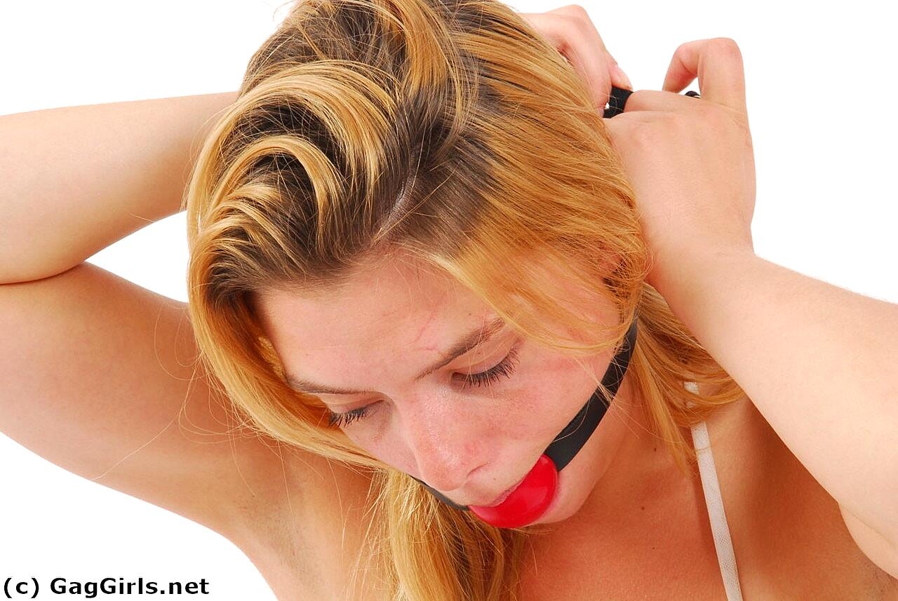 Blonde girl affixes a ball gag before donning stainless steel cuffs