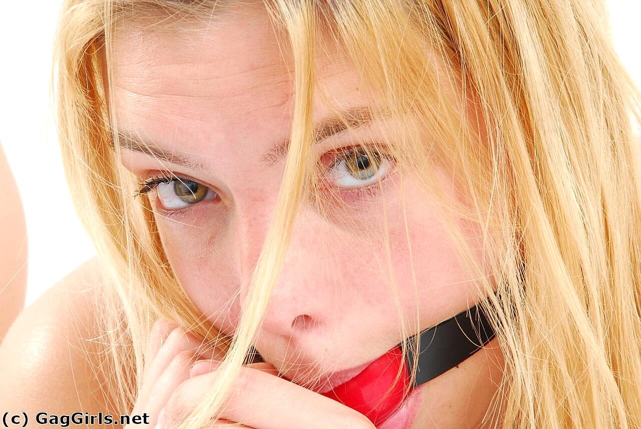 Blonde girl affixes a ball gag before donning stainless steel cuffs