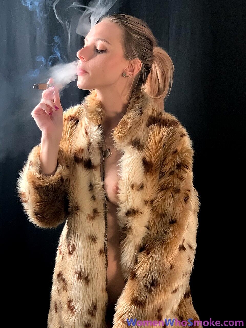 Blonde with a ponytail poses in her fur coat as she smokes a cigarette